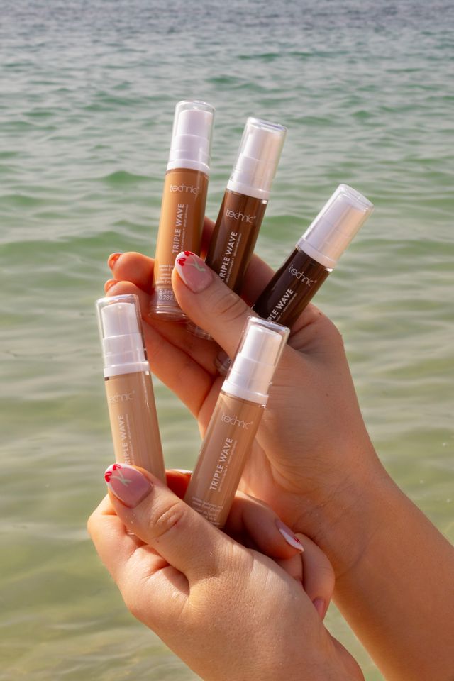 Female hands holding several shades of technic triple wave sundrenched concealers with beach water, background, natural summer glow