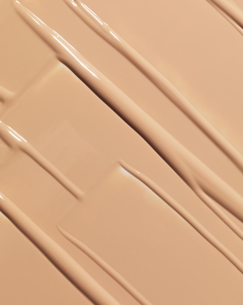 Close-up of a smooth beige cosmetic texture with glossy diagonal swatches and layered strokes or makeup foundation.
