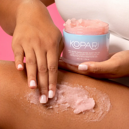 Person applying Kopari pink body scrub to their skin with a pink background