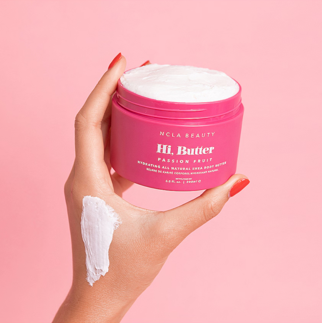 Hand holding a pink jar of NCLA Beauty Hi, Butter on a pink background