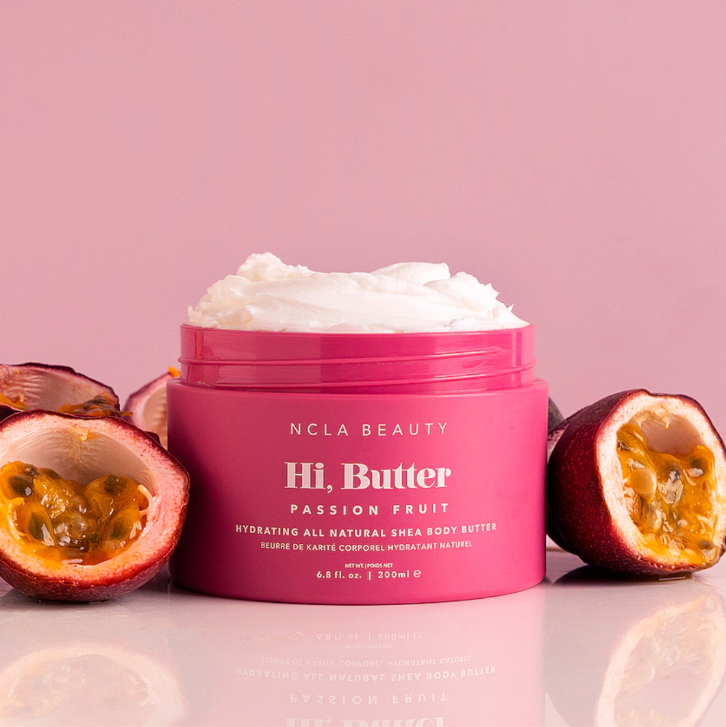 Pink jar of NCLA Beauty Hi, Butter Passion Fruit body butter with passion fruit halves on a pink background