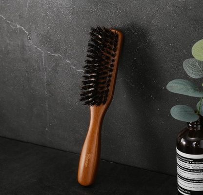 Ravego Boar Bristle Beard Brush on a dark surface with a plant in the corner